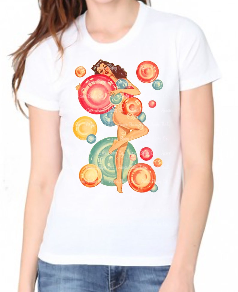 May include: A white short-sleeved t-shirt featuring a graphic print of a pin-up style figure surrounded by numerous colorful, translucent bubbles in shades of red, orange, yellow, and blue. The design is centered on the front of the garment.