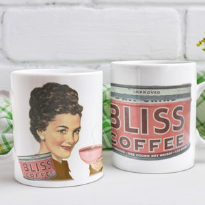 May include: Two white ceramic mugs with a retro design. One mug features a woman drinking coffee with a can of "Bliss Coffee" in the foreground. The other mug features a can of "Bliss Coffee" with the text "Improved" on the can.