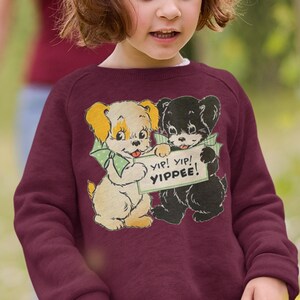 May include: A maroon sweatshirt with a vintage-style graphic of two cartoon dogs holding a sign that says "yip! yip! yippee!"