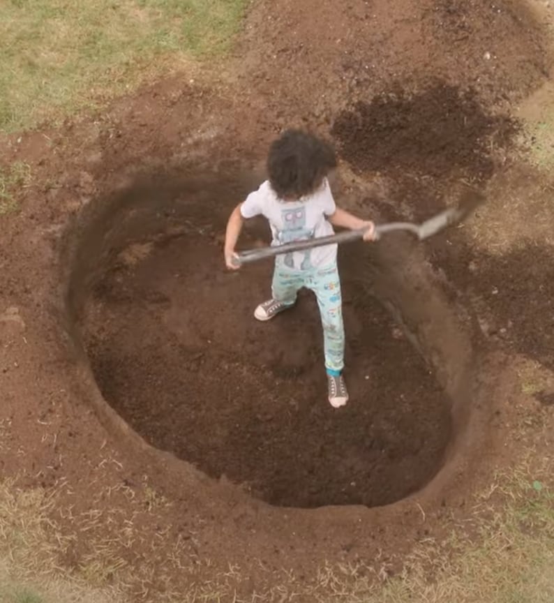 Puede incluir: Una persona est&aacute; cavando un gran agujero en el suelo con una pala. El agujero est&aacute; lleno de tierra y la persona lleva una camisa azul claro con un dise&ntilde;o de robot y pantalones azules y blancos.