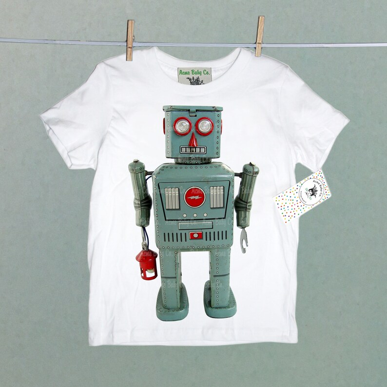Puede incluir: Camiseta blanca con un gr&aacute;fico de robot vintage. El robot es azul y gris con detalles rojos y una linterna en la mano. El texto "Acme Baby Co." est&aacute; en la camiseta.