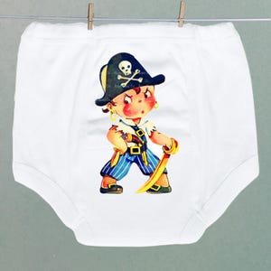 May include: White baby bodysuit with a cartoon pirate design. The pirate has a black hat with a skull and crossbones, a blue and white striped outfit, and a golden sword. The bodysuit is suspended on a clothesline.