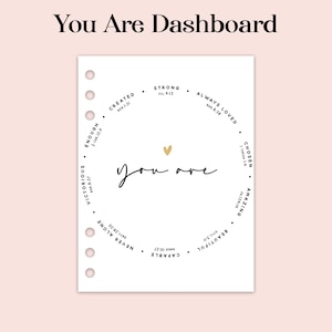 Può includere: Un inserto per planner bianco con le parole "You Are Dashboard" in alto. L'inserto presenta un design circolare con parole ispiratrici come "Strong" e "Amazing" sul bordo. Un cuore d'oro è al centro.