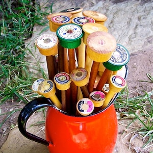 Może przedstawiać: Czerwony ceramiczny dzban wypełniony drewnianymi drutami do rob&oacute;tek ręcznych. Druty mają kolorowe etykiety z tekstem takim jak "Coats & Clarks" i "Bollfas".