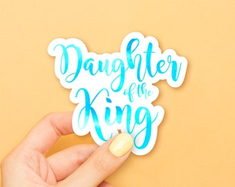 Op de afbeelding: Een witte sticker met blauwe aquarelletters met de tekst "Dochter van de Koning".