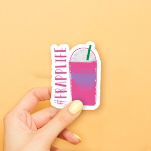 May include: A white sticker with a pink and purple iced coffee drink with a green straw and the text "#FRAPPLIFE" in pink.