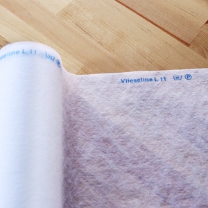 May include: A white roll of Vlieseline L 11 interfacing fabric with a blue label that says "Vlieseline L 11" and a washing instruction symbol.