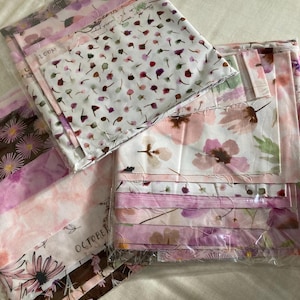 May include: A collection of floral fabric bundles in pink, white, and brown hues. The fabrics display diverse floral patterns, including daisies and abstract designs. Some bundles are labelled with the words "LOOM" and "OCTOBER".