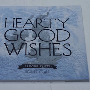 May include: A blue book with the title "HEARTY GOOD WISHES - COASTAL QUILTS - BY JANET CLARE" on the cover.