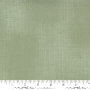 May include: A solid sage green fabric with a subtle texture. The fabric is measured in inches with a ruler.
