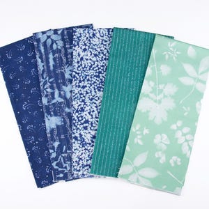 May include: A set of six fabric swatches in shades of blue and green. The fabrics feature different patterns, including floral, geometric, and abstract designs.