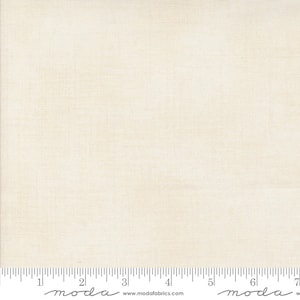 May include: Cream-coloured fabric with a subtle woven texture. A ruler is placed along the bottom edge, marked with inch increments. The fabric appears to be a solid colour, suitable for quilting or other craft projects.