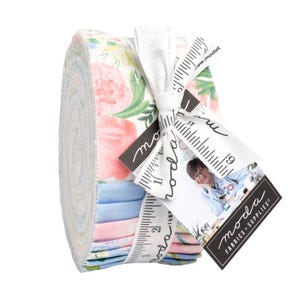 May include: A rolled bundle of floral fabric in shades of pink, blue, and green, tied with a white ribbon printed with ruler markings and the words "moda fabrics + supplies". A tag with a photo and the brand name is attached.