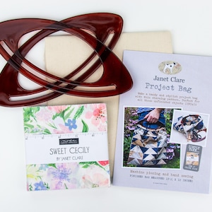 Op de afbeelding: Een naaiprojectset met een donkerbruine, in elkaar grijpende handgreep, stoffen vierkanten, een projecttassenpatroon en een stuk canvas. De stoffen vierkanten zijn gemarkeerd met "Sweet Cecily". De tas meet 31,75 cm x 25,4 cm.
