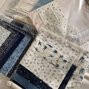 Peut inclure: Assortiment de morceaux de tissu aux motifs et couleurs variés, dont le bleu, le blanc et le gris. Certains tissus présentent des formes géométriques, des oiseaux et des rayures. Les pièces sont emballées dans du plastique transparent.