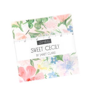May include: A stack of fabric squares with a floral pattern in pink, blue, and green. The fabric is labeled "Sweet Cecily by Janet Clare" with a ruler printed on the top. The fabric squares are likely for quilting or other craft projects.