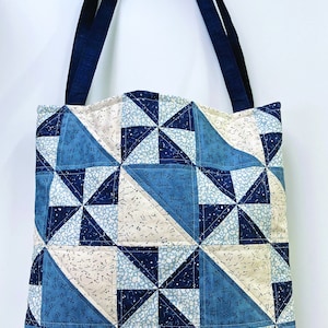 Op de afbeelding: Een blauwe en witte patchwork tote bag met een geometrisch patroon. De tas heeft twee zwarte banden.