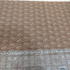 Peut inclure: Tissu marron avec un motif répétitif de vignes et de feuilles crème. Une règle transparente avec des marquages en pouces est placée en bas du tissu. Le tissu est enroulé sur le côté droit.