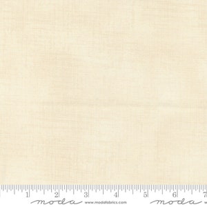 Könnte beinhalten: Nahaufnahme eines cremefarbenen Stoffes mit einer dezenten gewebten Textur. Der Stoff ist mit einem Zollstock in Zoll gekennzeichnet und das Wort "moda" erscheint zweimal auf dem Zollstock.