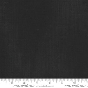 May include: A solid black fabric swatch with a subtle texture. The fabric is measured with a ruler in inches, with the word "moda" printed on the ruler.