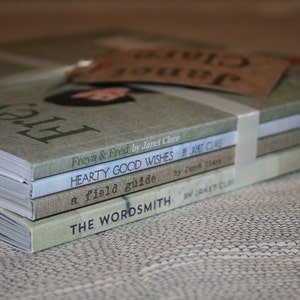 Pode incluir: Uma pilha de quatro livros com capas verdes, brancas e marrons. O livro de cima é intitulado "Freya & Fred" de Janet Clare. O segundo livro é intitulado "Hearty Good Wishes" de Janet Clare. O terceiro livro é intitulado "A Field Guide" de Janet Clare. O livro de baixo é intitulado "The Wordsmith" de Janet Clare.
