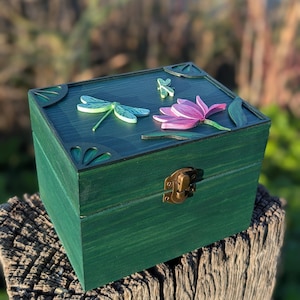 May include: A green wooden box with a hinged lid and a brass latch. The top of the box is decorated with a pink flower and two green dragonflies.
