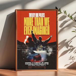 Op de afbeelding: Een ingelijste poster met een rode achtergrond toont de tekst "TWENTY ONE PILOTS MORE THAN WE EVER IMAGINED" in het geel. De poster toont silhouetten van bandleden die live optreden in Mexico City. De onderste tekst luidt "EXPERIENCE IT IN IMAX® AND CINEMAS WORLDWIDE FROM FEBRUARY 26".