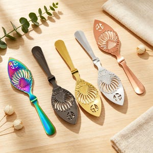 May include: Five metal absinthe spoons arranged in a row, featuring a decorative shell-like cutout pattern. The spoons are finished in iridescent rainbow, matte black, polished gold, polished silver, and rose gold metallic colours respectively.