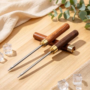 May include: Two ice picks with long, pointed stainless steel tips and cylindrical wooden handles. The handles feature gold-coloured metal ferrules and are engraved with the text "Neil Hare" and "The Breathtaking" in a cursive script font.