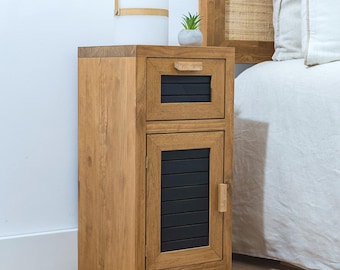 May include: A wooden nightstand with a black drawer and a black door with a slatted design. The nightstand is next to a bed with a white linen headboard and a white linen duvet.