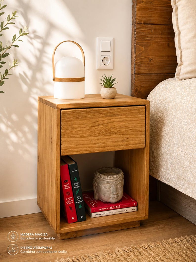 May include: A rectangular wooden nightstand featuring a single top drawer and an open lower shelf. The shelf contains two upright books, a horizontal book, and a gray stone-like sculpture of a human head. The wood has a natural grain finish.