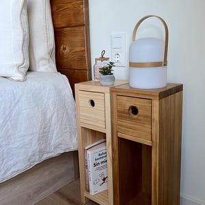 May include: Two wooden bedside tables with drawers and shelves, one with a book titled "Sin miedo" and the other with a white lamp with a wooden handle.