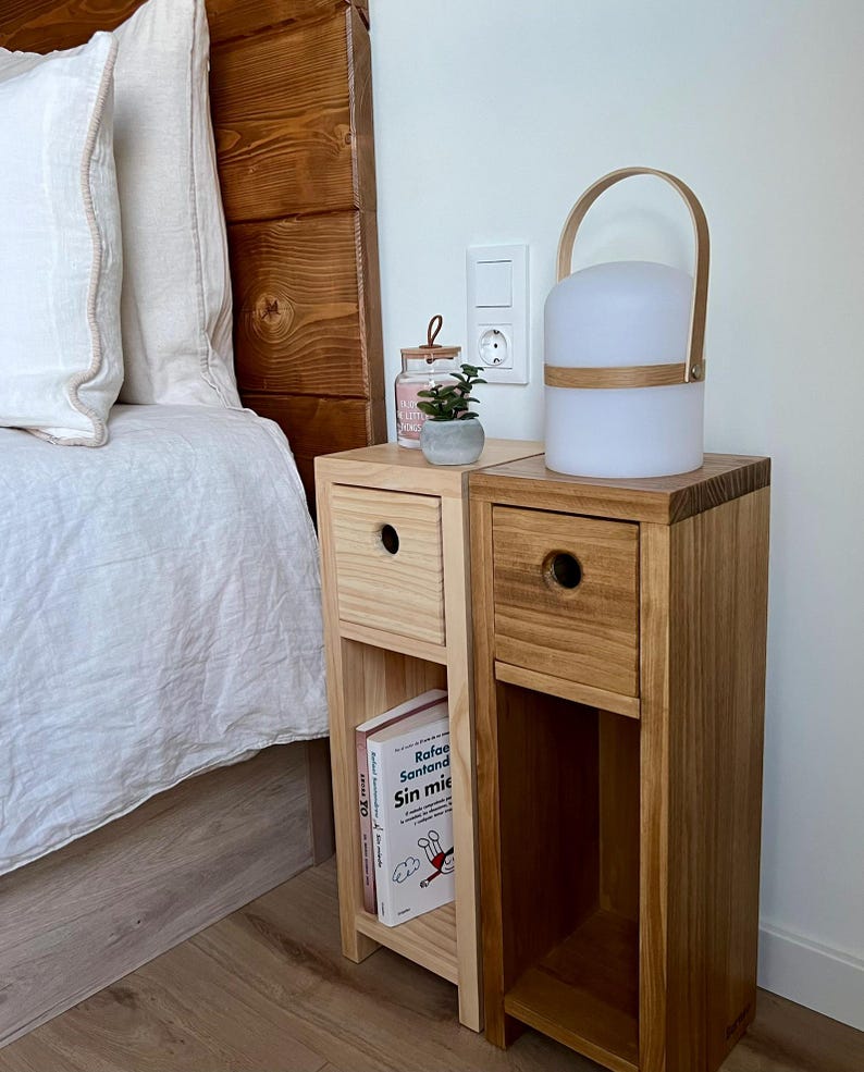May include: Two wooden bedside tables with drawers and shelves, one with a book titled "Sin miedo" and the other with a white lamp with a wooden handle.