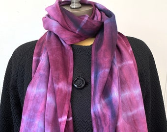May include: A purple and blue tie-dye silk scarf with a white background. The scarf is folded and draped over a black jacket.