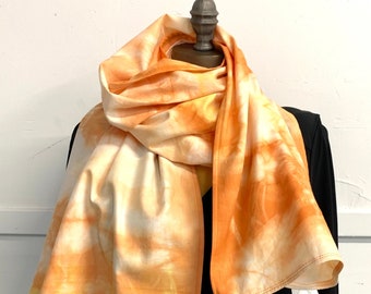 May include: A long, orange and yellow tie-dye scarf with a white background. The scarf is draped over a black dress form.