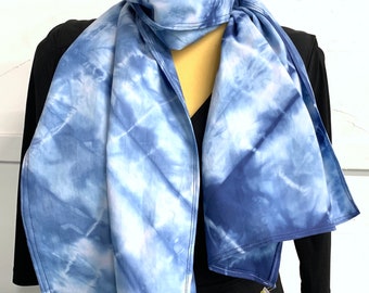 May include: A blue and white tie-dye scarf with a diagonal pattern. The scarf is folded and displayed on a mannequin.