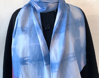 May include: A light blue scarf with a tie-dye pattern. The scarf is folded in half and draped over a black jacket.