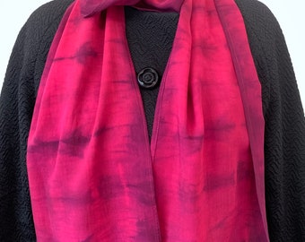 May include: A long, thin, pink and purple silk scarf with a tie-dye pattern. The scarf is draped around a mannequin's neck.