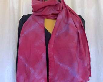 May include: A rectangular scarf featuring a tie-dye pattern in shades of deep magenta and soft lavender. The fabric is draped around a mannequin, displaying a repeating circular motif across the length of the material with finished edges.