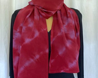 May include: A rectangular scarf featuring a deep red base color with diagonal, soft-edged streaks of muted purple throughout the fabric. The scarf is draped around a mannequin, displaying a smooth texture and a consistent, flowing drape across the front.