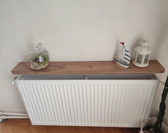 May include: A white radiator with a wooden shelf above it. The shelf is decorated with a glass terrarium, a small sailboat, and a white lantern.
