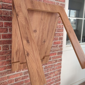 Könnte beinhalten: Ein klappbarer Holztisch mit brauner Holzmaserung. Der Tisch ist zusammengeklappt und an einer Backsteinwand angelehnt.