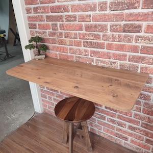 Może przedstawiać: Drewniany stolik ścienny z zaokrąglonym brzegiem i mały drewniany stołek. Stolik jest zamontowany na ścianie z cegły i ma na nim mały bonsai w doniczce.