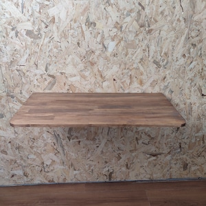 Peut inclure: Un bureau flottant rectangulaire fix&eacute; au mur, dot&eacute; d'une surface en bois brun fonc&eacute; au grain lisse et aux coins arrondis. Le bureau est fix&eacute; sur un mur recouvert de panneaux de particules orient&eacute;es clairs, cr&eacute;ant un contraste de tons.