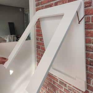 May include: White folding table mounted on a brick wall. The table is folded up and secured with metal hinges.
