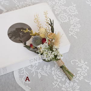 May include: A small bouquet of dried flowers tied with twine. The bouquet includes white, red, and yellow flowers, as well as dried grasses.