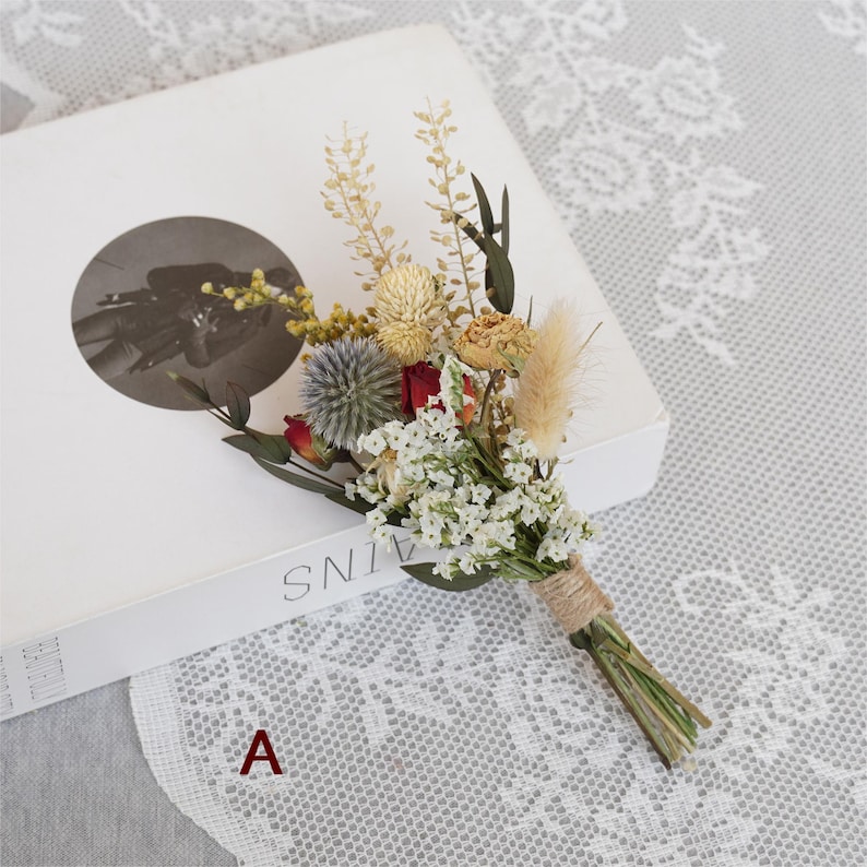 May include: A small bouquet of dried flowers tied with twine. The bouquet includes white, red, and yellow flowers, as well as dried grasses.