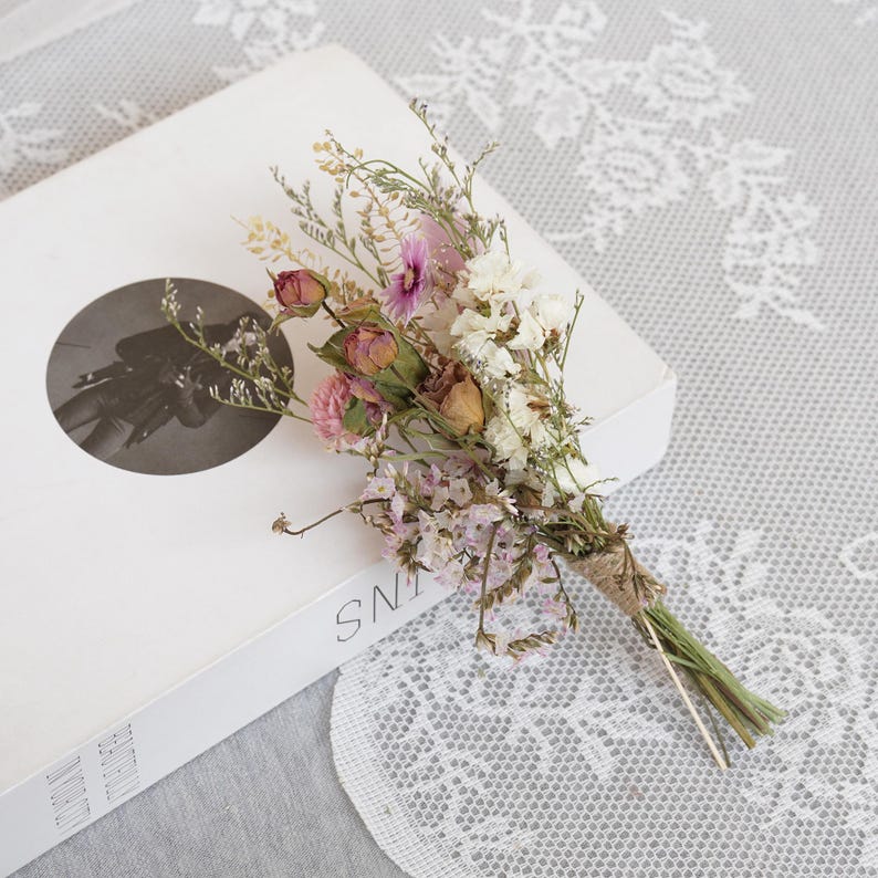 May include: A small bouquet of dried flowers tied with twine. The bouquet includes pink, white, and brown flowers, and green stems.