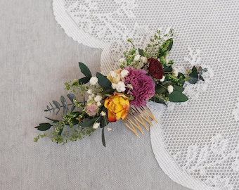 May include: A floral hair comb with dried flowers in shades of pink, yellow, and green. The comb is made of wood and has a natural finish.