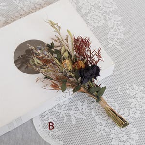 May include: A small bouquet of dried flowers with black, yellow, and brown flowers, and green leaves. The bouquet is tied with twine.